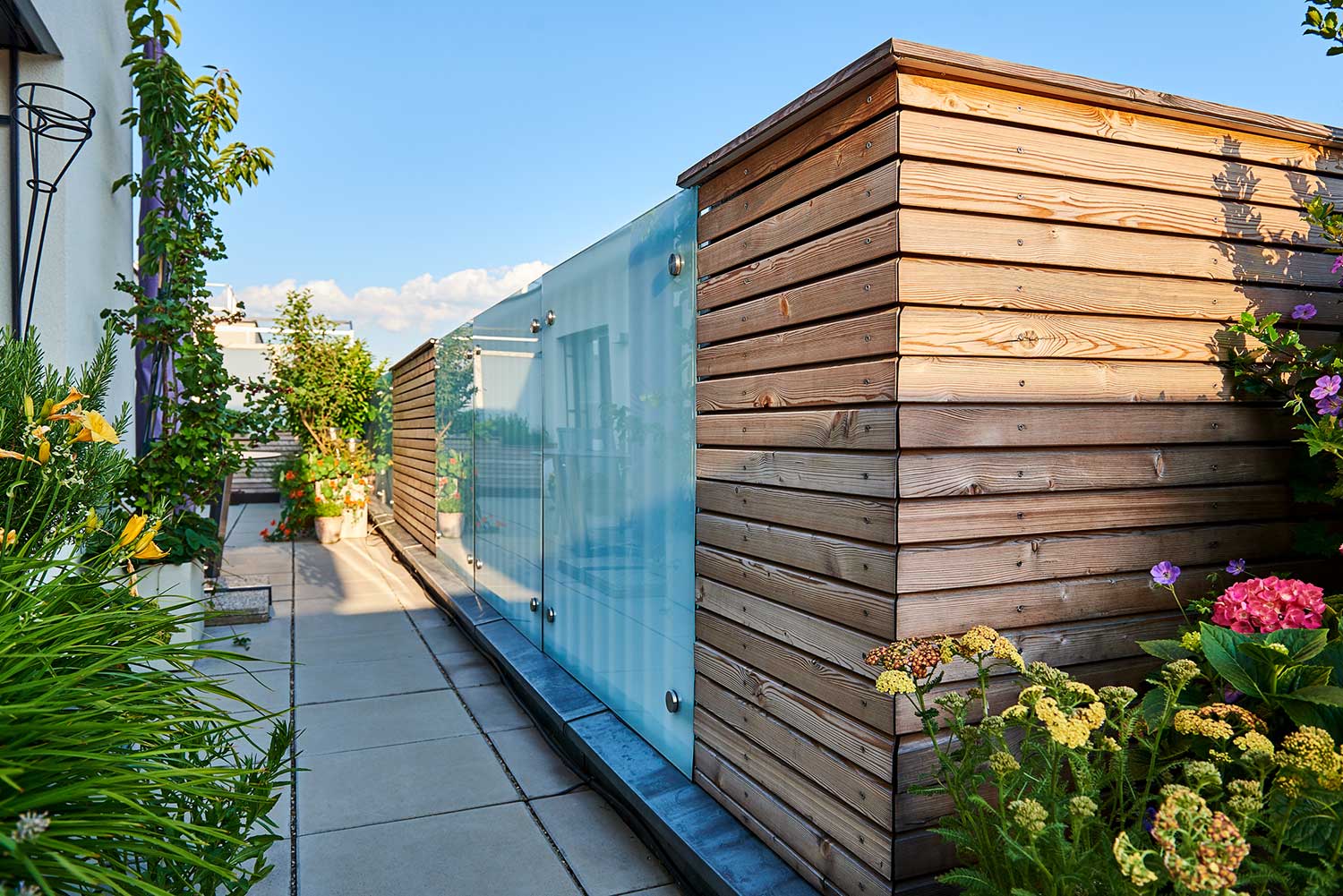 Eine begrünte Dachterrasse mit einer Wand aus Holz und Glaselementen